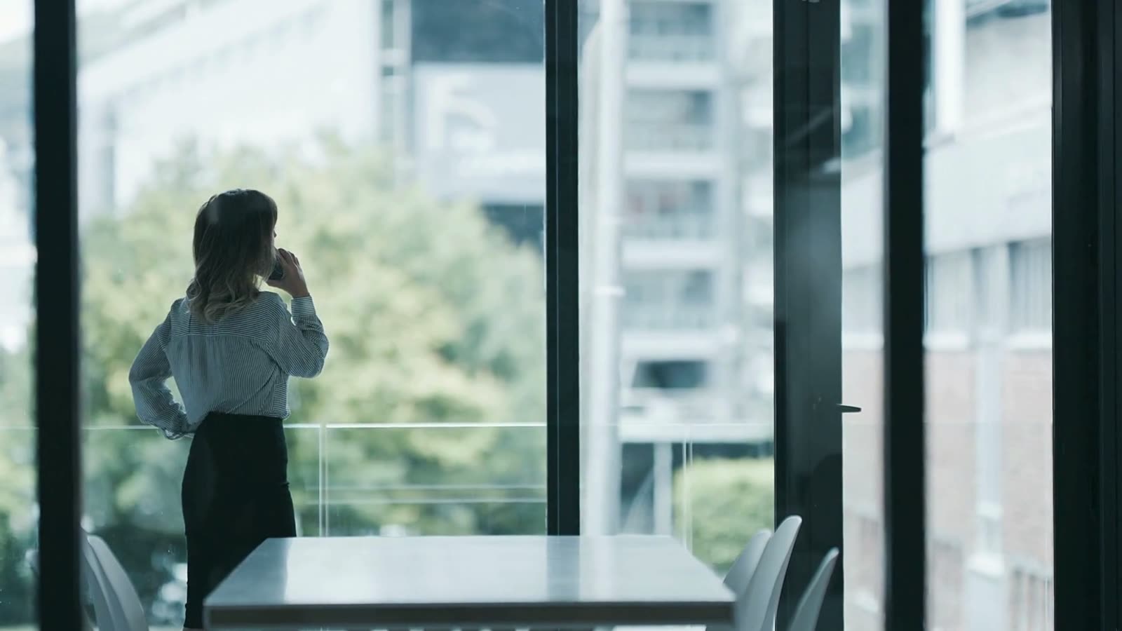 A woman on the phone by the window of a glass-walled office