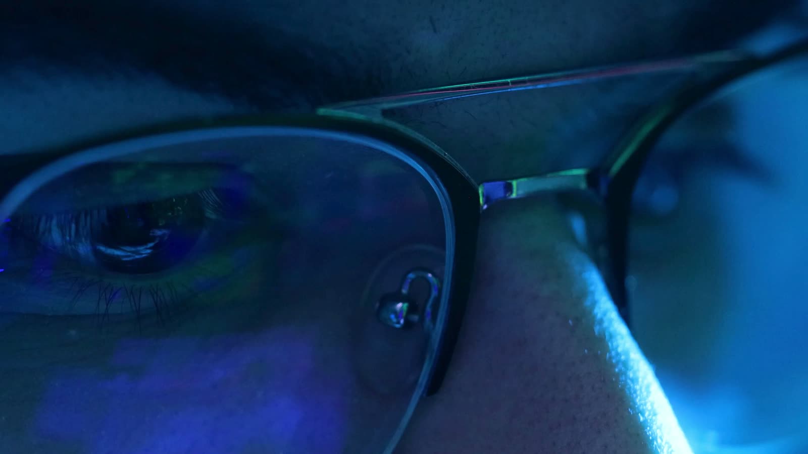 A close view of an eye behind glasses, lit by the reflection of a screen